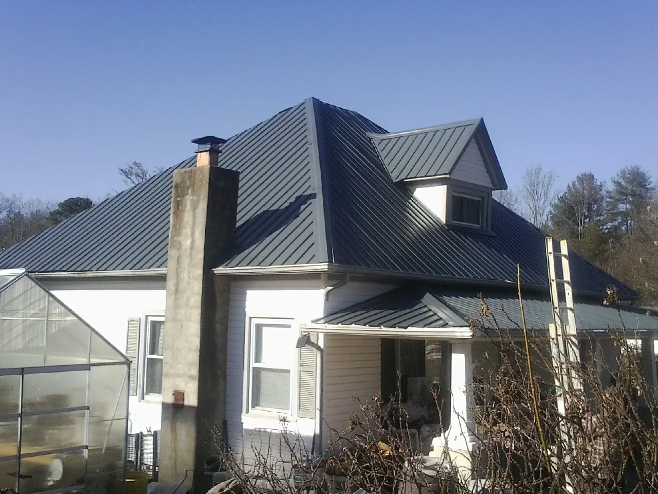 Dark blue standing seam metal roof on a white farmhouse with dormer — Slate & Tile Roof Repair by Roofing Brothers in Waynoka