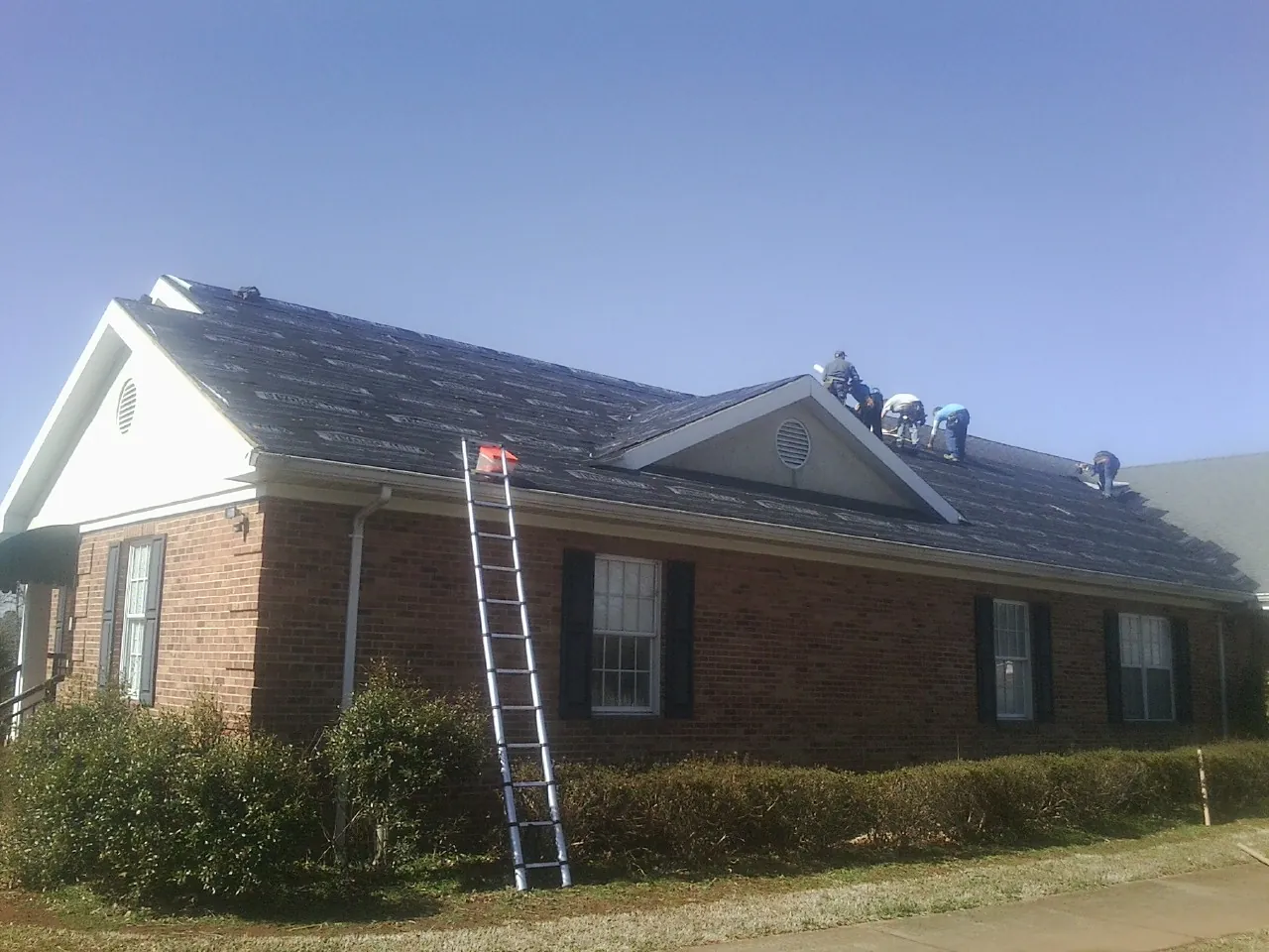 Crew tearing shingles off a brick ranch roof with a ladder set — Emergency Roof Repair work by our crew in Waynoka
