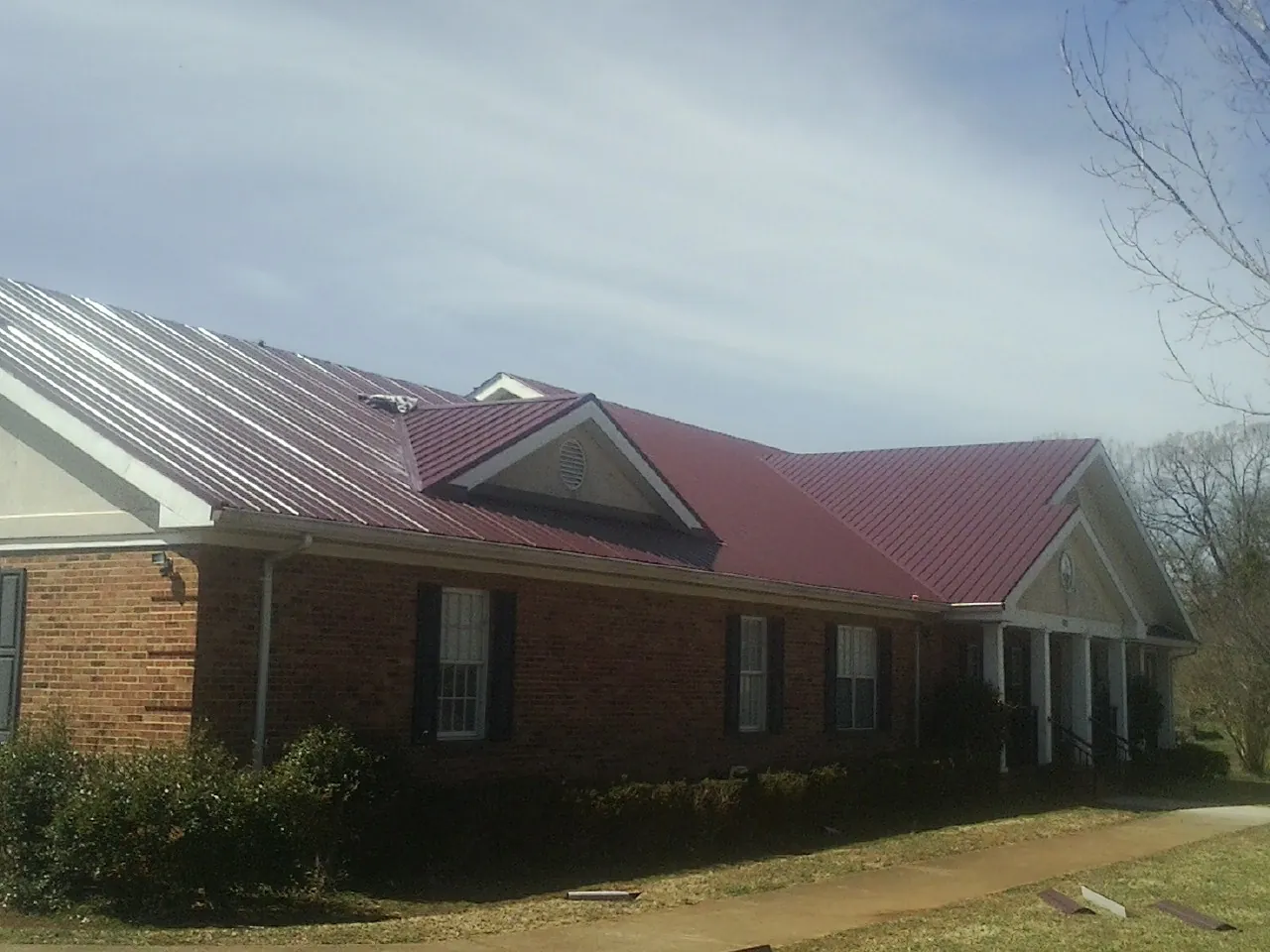Red metal roof with gabled entries on a long brick building, from a Hail Damage Roof Repair job in Waynoka