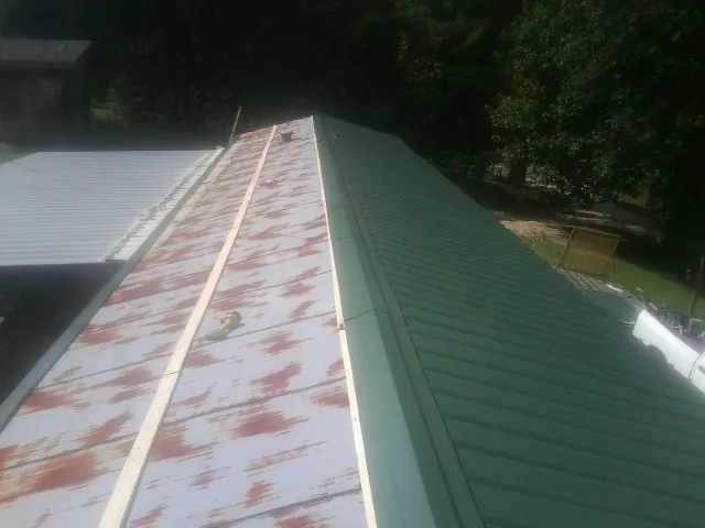 Old rusted panels beside newly installed green metal roofing — Wind Damage Roof Repair by Roofing Brothers in Waynoka