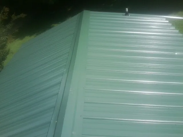 New green metal panels meeting at the ridge of a roof — Flat Roof Repair work by our crew in Waynoka