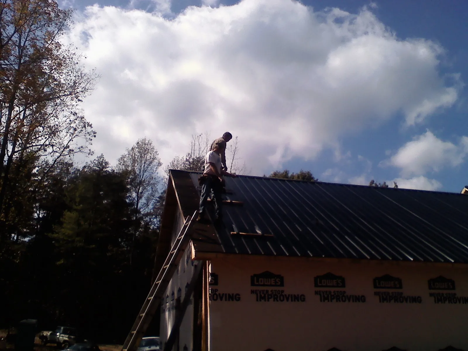 Roofer fastening dark metal panels high against a cloudy sky, from a Roof Inspection job in Waynoka