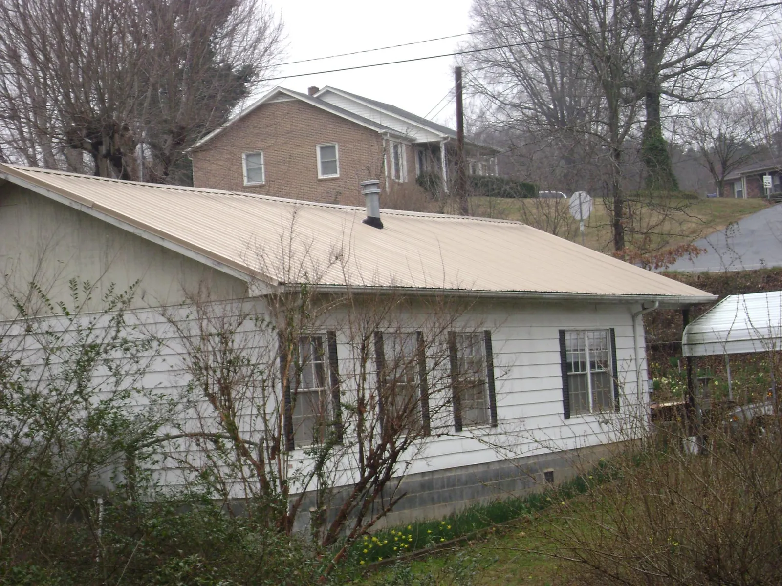 Tan metal roof on a white sided house set into a hillside — Commercial Roofing by Roofing Brothers in Waynoka