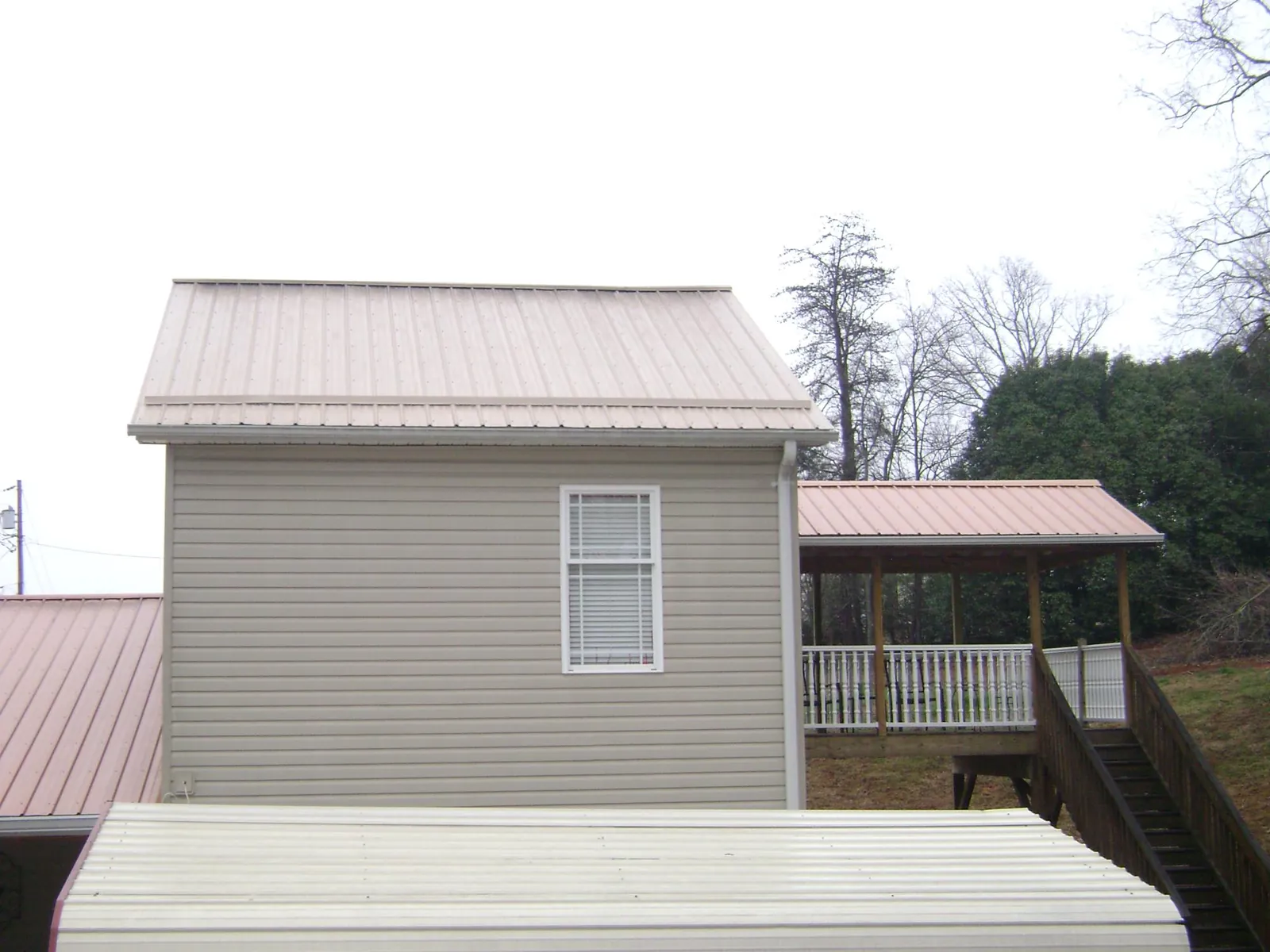 Tan metal roofs on a two story addition and attached porch, from a Roof Replacement job in Waynoka